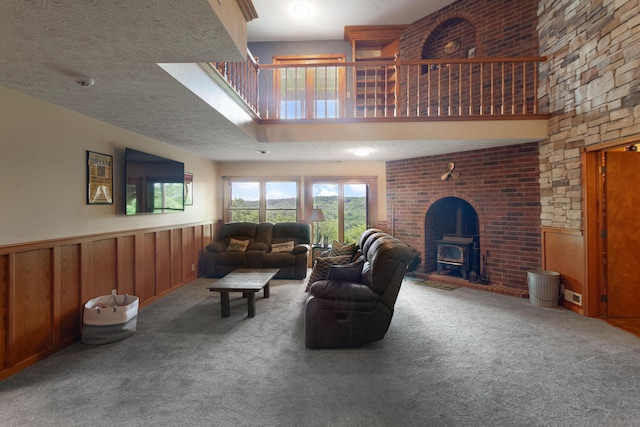 carpeted living area with a high ceiling, a wood stove, and a wainscoted wall