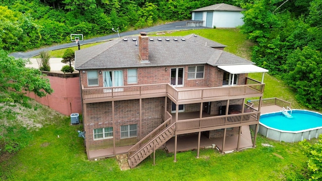 back of property with a chimney, brick siding, a wooden deck, a lawn, and an outdoor pool