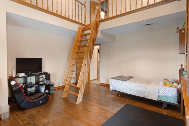 bedroom with baseboards, wood finished floors, and a towering ceiling