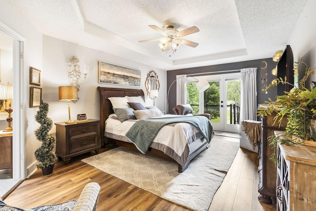 bedroom with a raised ceiling, ceiling fan, hardwood / wood-style flooring, and access to outside