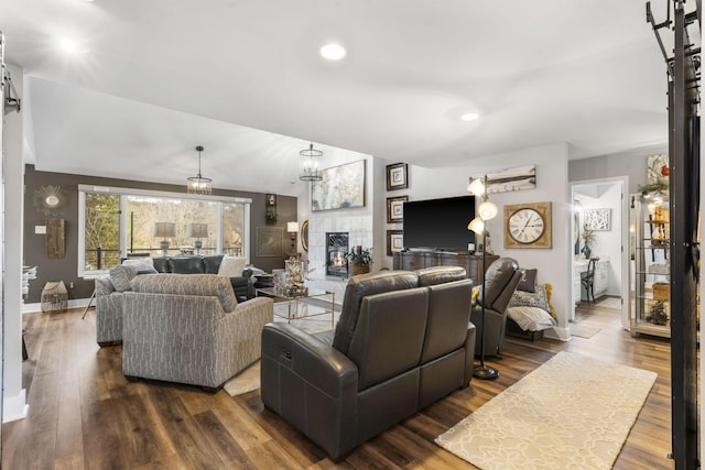 living room with a notable chandelier, dark wood-type flooring, a tile fireplace, and vaulted ceiling