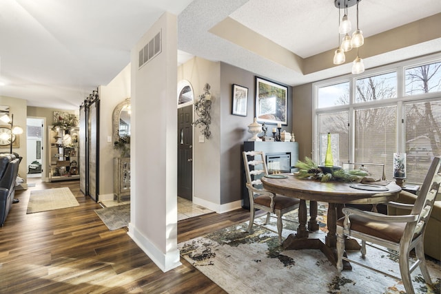 dining room with a raised ceiling, a textured ceiling, dark hardwood / wood-style floors, and an inviting chandelier