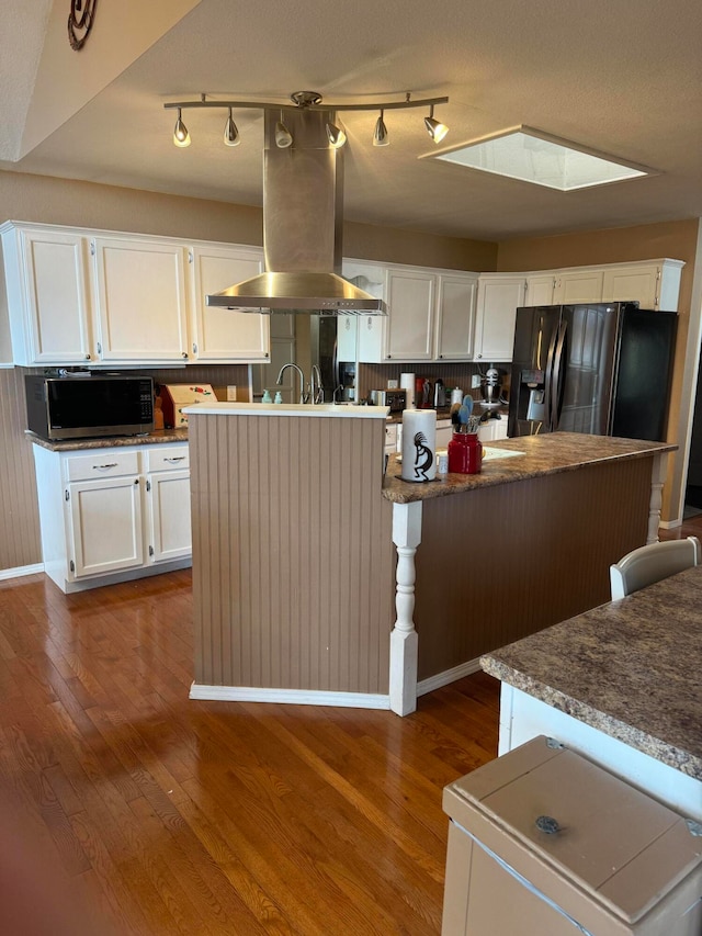 kitchen with a skylight, white cabinetry, island exhaust hood, a center island, and fridge with ice dispenser