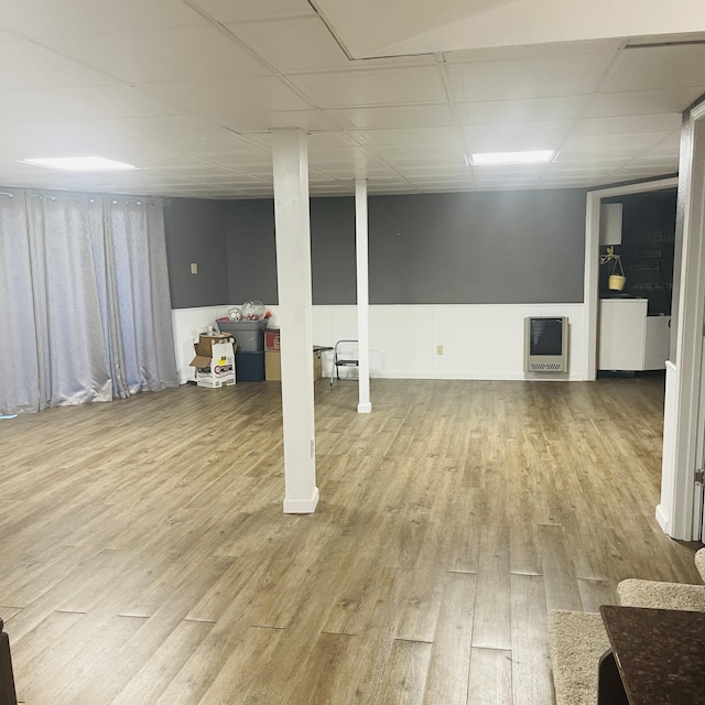 basement with a drop ceiling, heating unit, and light wood-type flooring