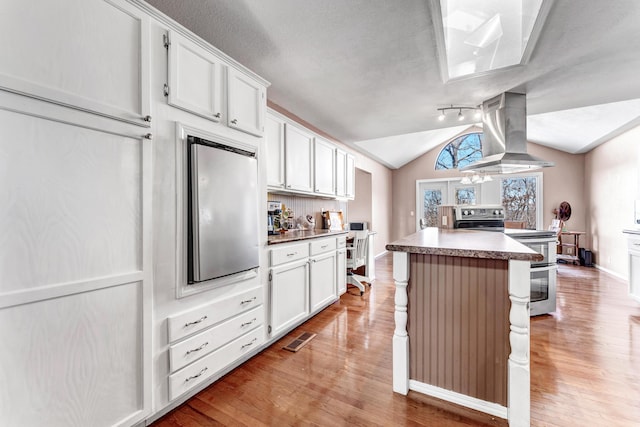 kitchen with range with two ovens, a kitchen island, visible vents, vaulted ceiling, and ventilation hood