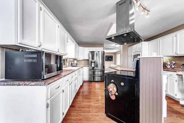 kitchen featuring black microwave, stainless steel fridge with ice dispenser, island exhaust hood, white cabinetry, and a sink