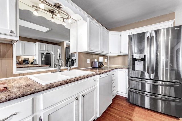 kitchen with white dishwasher, a skylight, a sink, white cabinetry, and stainless steel fridge with ice dispenser