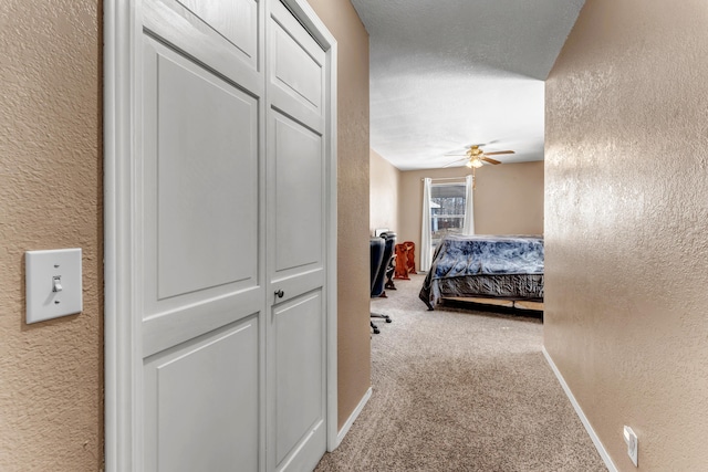 bedroom with carpet, a textured wall, a ceiling fan, a textured ceiling, and baseboards