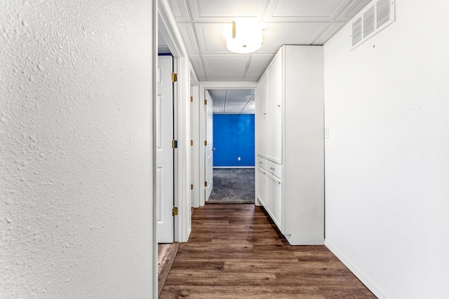 hall with a textured wall, wood finished floors, and visible vents