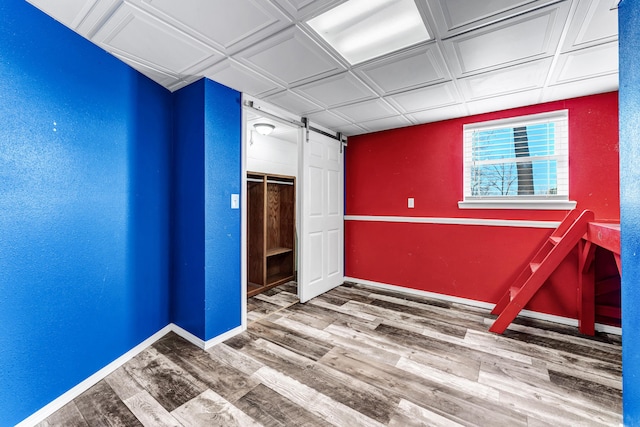 empty room with a barn door, baseboards, a textured wall, an ornate ceiling, and wood finished floors