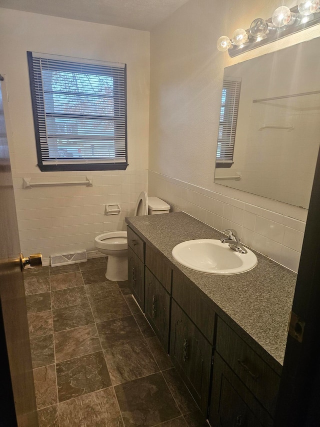 bathroom with toilet, tile walls, and vanity