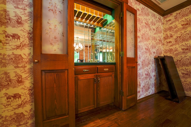 bar with dark wood-type flooring, ornamental molding, and a chandelier