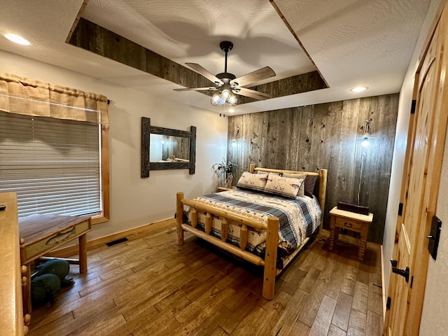 bedroom with hardwood / wood-style flooring, ceiling fan, wood walls, and a textured ceiling