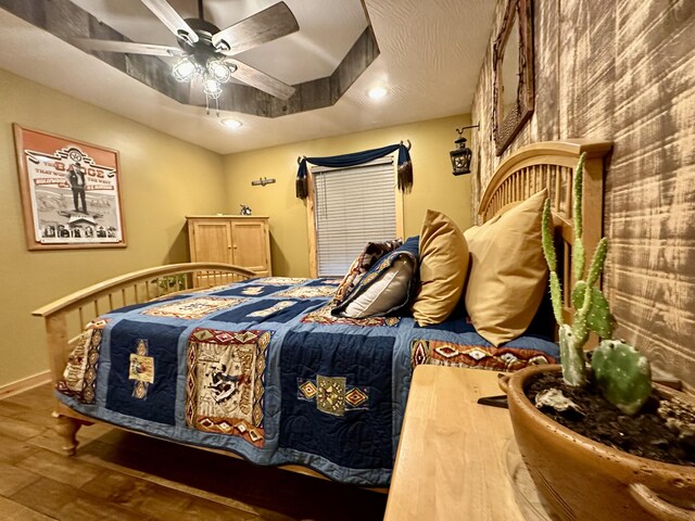 bedroom featuring ceiling fan, a raised ceiling, and wood-type flooring