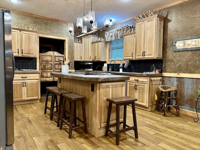 kitchen with ornamental molding, a kitchen island, appliances with stainless steel finishes, light brown cabinetry, and light hardwood / wood-style floors