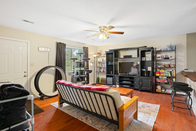 living room featuring ceiling fan, hardwood / wood-style flooring, and a textured ceiling