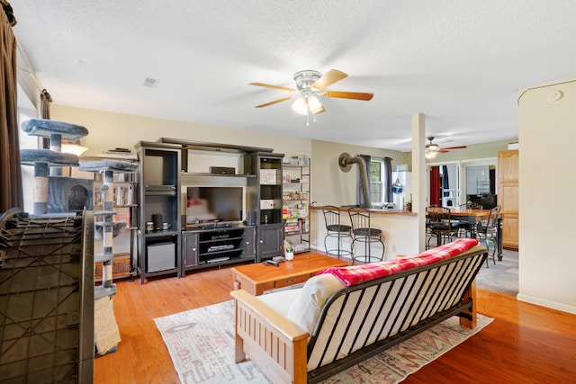 living room with a textured ceiling, ceiling fan, and light hardwood / wood-style flooring