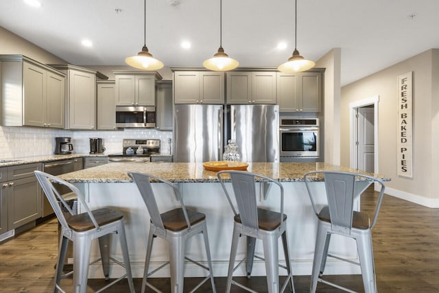 kitchen featuring a kitchen island, dark hardwood / wood-style flooring, decorative light fixtures, appliances with stainless steel finishes, and a kitchen bar