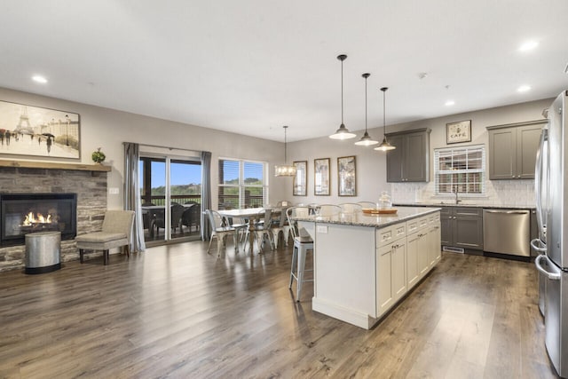 kitchen with a center island, stainless steel appliances, hanging light fixtures, gray cabinets, and a kitchen bar