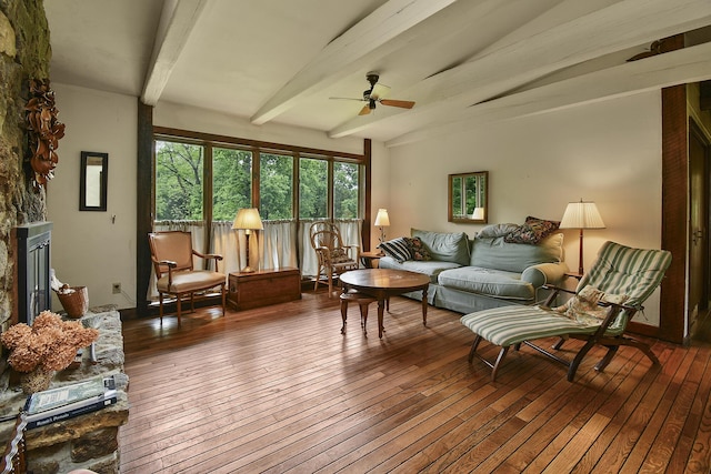 living room featuring ceiling fan, a stone fireplace, beam ceiling, and hardwood / wood-style floors