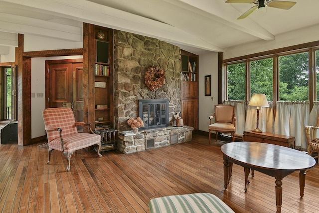 living area featuring wood-type flooring, a stone fireplace, a ceiling fan, and lofted ceiling with beams