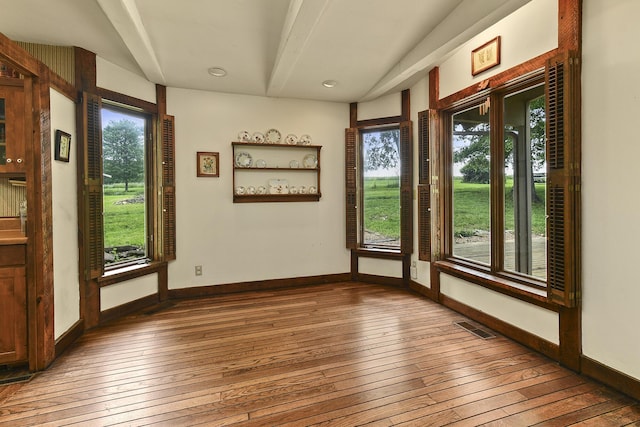 interior space featuring hardwood / wood-style floors, baseboards, visible vents, and beam ceiling