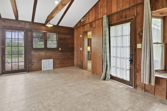 empty room featuring visible vents, wood walls, and lofted ceiling with beams