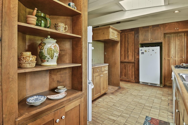 kitchen featuring open shelves, freestanding refrigerator, light countertops, and brown cabinets