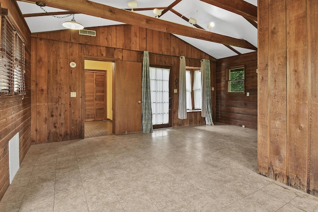 empty room with visible vents, wood walls, and vaulted ceiling with beams
