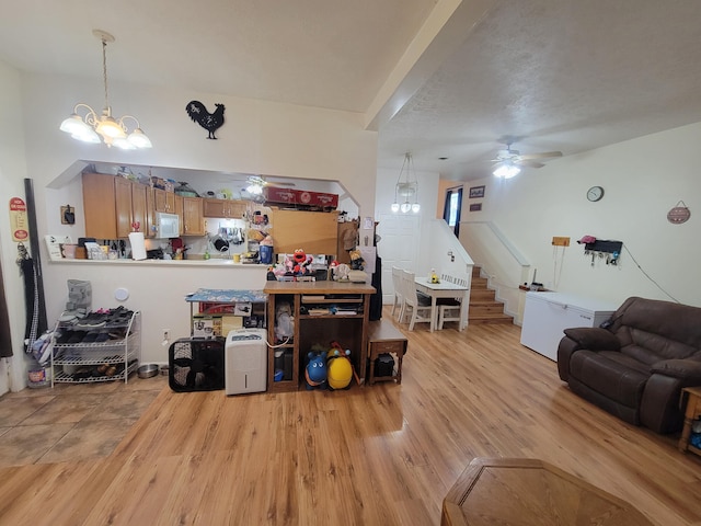 living room with ceiling fan with notable chandelier, a textured ceiling, and light wood-type flooring