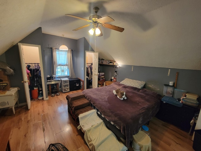 bedroom featuring ceiling fan, lofted ceiling, wood-type flooring, a walk in closet, and a closet