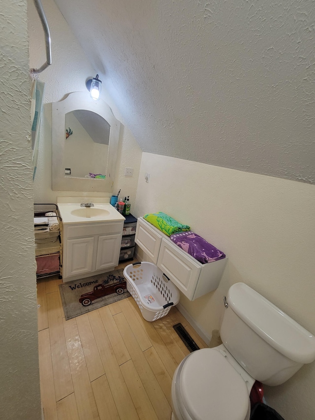 bathroom with toilet, wood-type flooring, lofted ceiling, vanity, and a textured ceiling