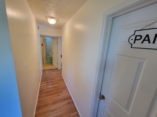 hallway with a textured ceiling and light hardwood / wood-style floors