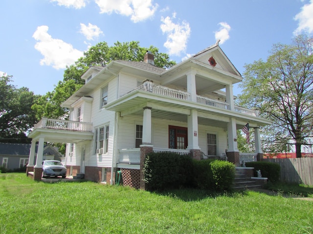 greek revival house with a front yard, a balcony, and a porch