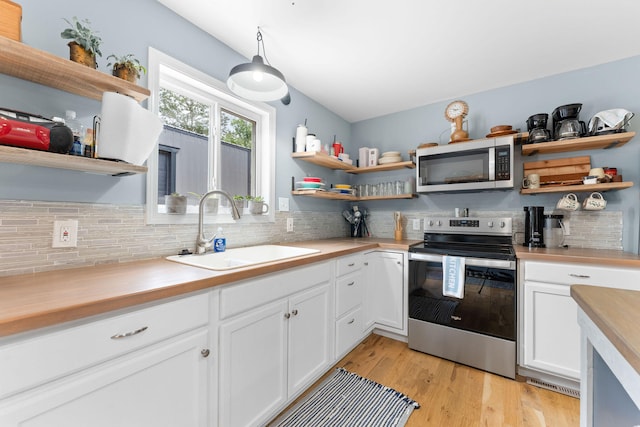 kitchen featuring light wood-type flooring, sink, hanging light fixtures, white cabinetry, and appliances with stainless steel finishes