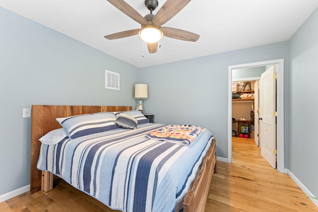 bedroom with ceiling fan, light hardwood / wood-style flooring, and a walk in closet