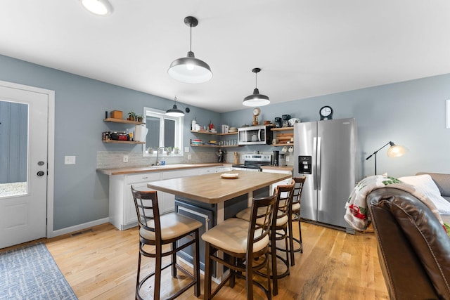 kitchen featuring appliances with stainless steel finishes, pendant lighting, light hardwood / wood-style floors, and white cabinets