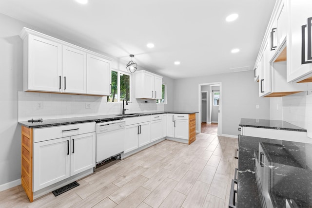 kitchen with light hardwood / wood-style flooring, dark stone countertops, sink, white dishwasher, and white cabinetry