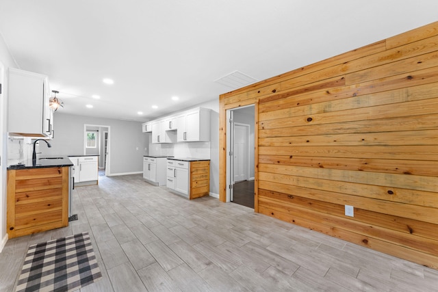 kitchen featuring wood walls, light hardwood / wood-style floors, white cabinets, and sink