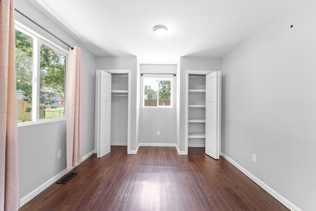 unfurnished bedroom featuring two closets, dark hardwood / wood-style flooring, and multiple windows