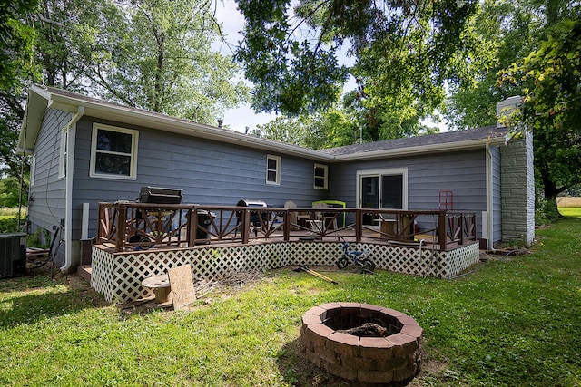 rear view of property with central AC unit, a wooden deck, a yard, and an outdoor fire pit