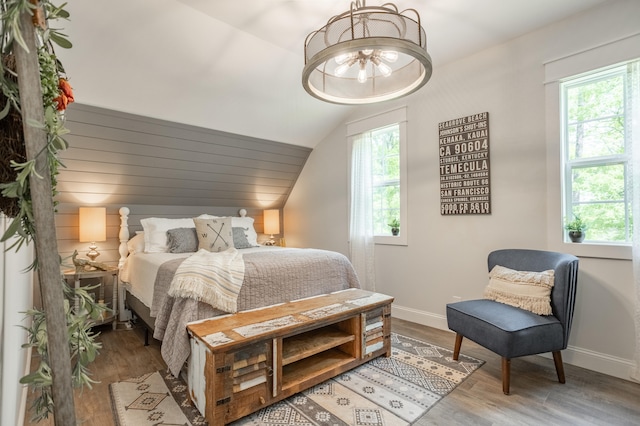 bedroom featuring wood-type flooring, vaulted ceiling, an inviting chandelier, and multiple windows