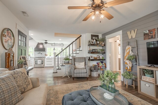 living room with ceiling fan, wood walls, and wood-type flooring