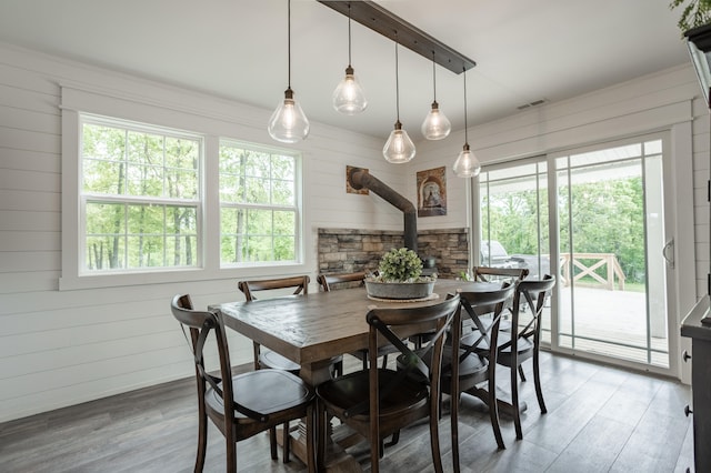 dining area with wood-type flooring, wooden walls, and a wood stove