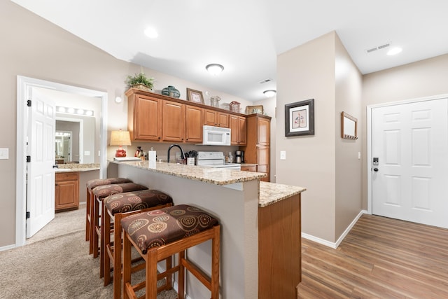 kitchen with light stone countertops, wood-type flooring, a breakfast bar, white appliances, and kitchen peninsula