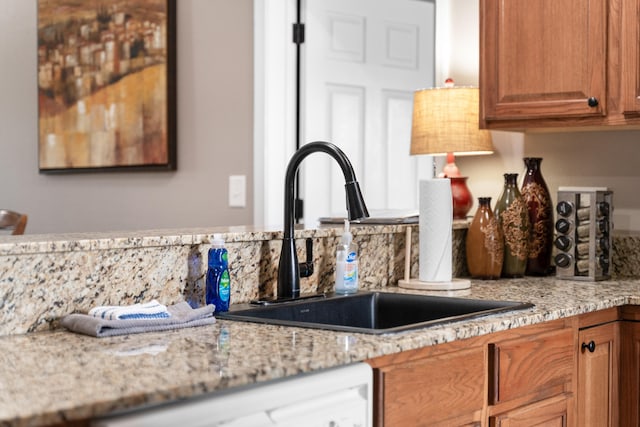 room details with light stone countertops, brown cabinetry, white dishwasher, and a sink