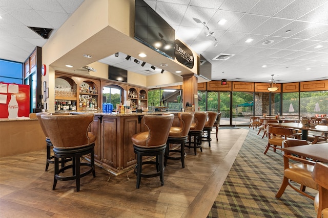 bar featuring wood-type flooring, a wealth of natural light, a drop ceiling, and a community bar
