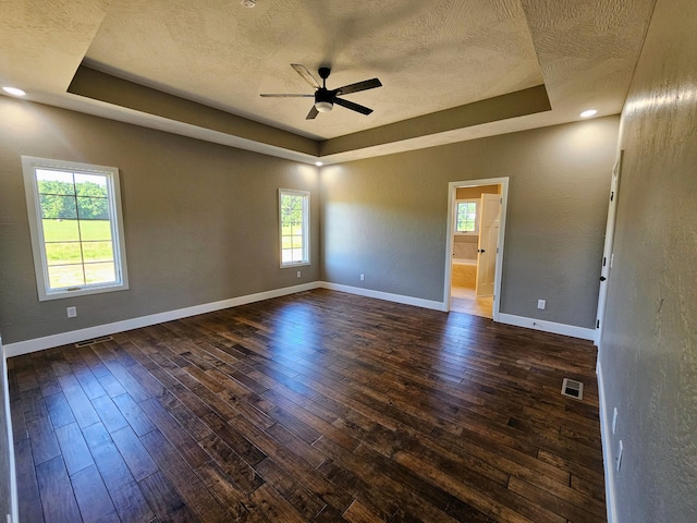 unfurnished room featuring ceiling fan, a tray ceiling, dark hardwood / wood-style floors, and a textured ceiling