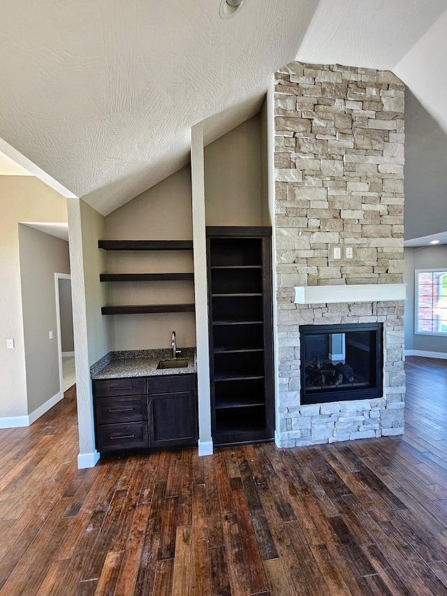 unfurnished living room with lofted ceiling, dark wood-type flooring, sink, a fireplace, and a textured ceiling