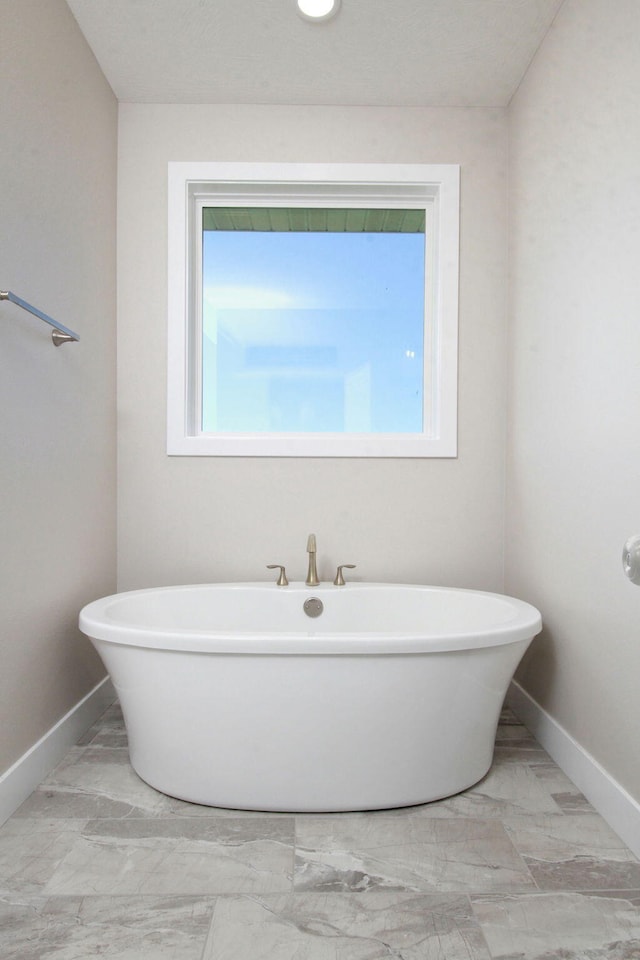 full bathroom with a soaking tub, a healthy amount of sunlight, and baseboards